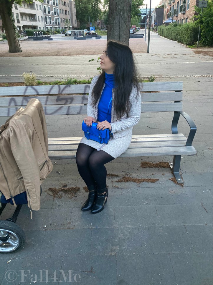 A beige skirt suit in French tweed worn with black accessories and an azure blue turtleneck and bag.