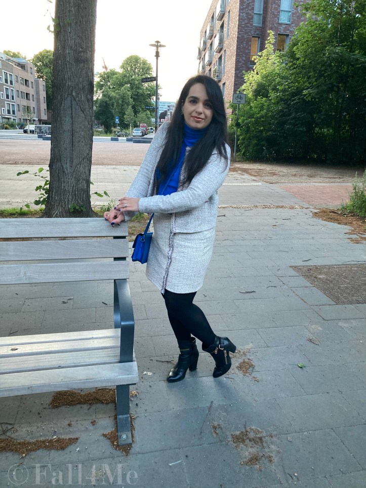A beige skirt suit in French tweed worn with black accessories and an azure blue turtleneck and bag.