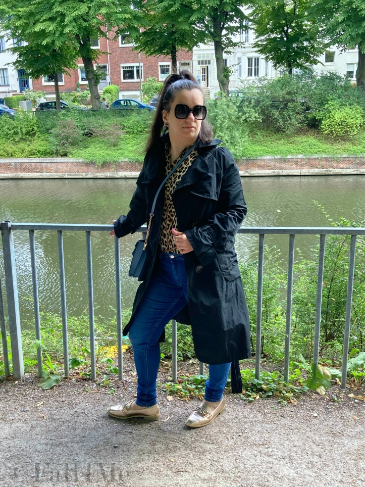 A black trench coat worn with skinny jeans and a leopard printed blouse.