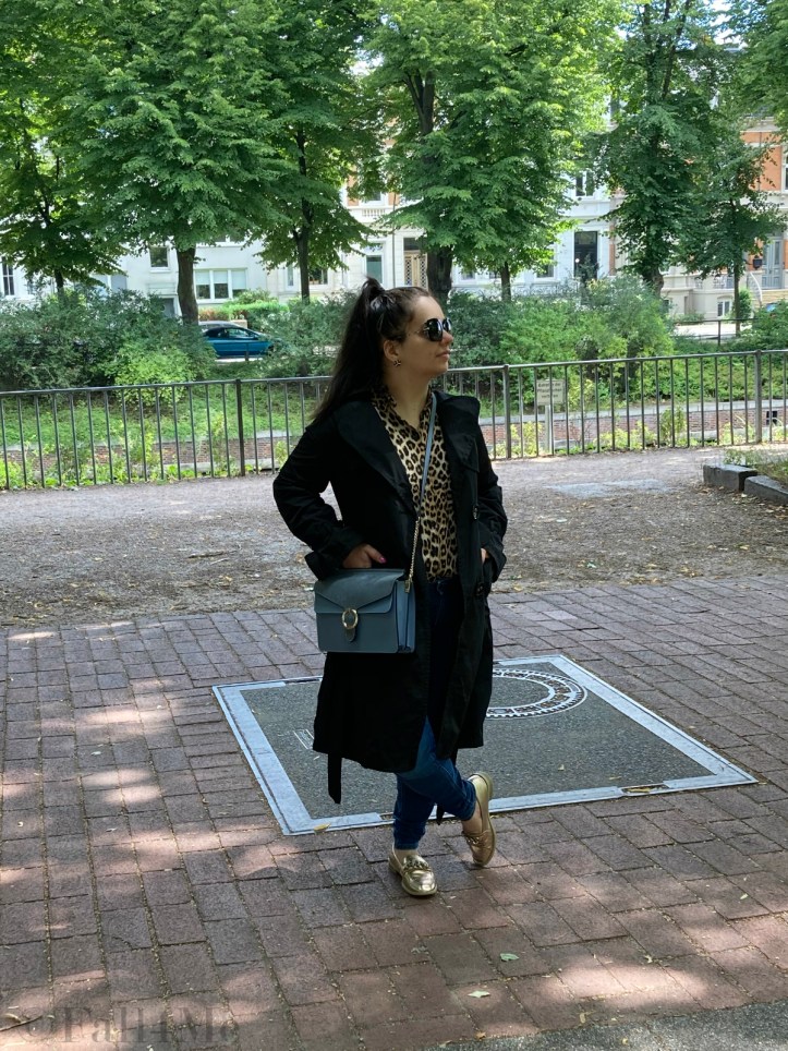 A black trench coat worn with skinny jeans and a leopard printed blouse.