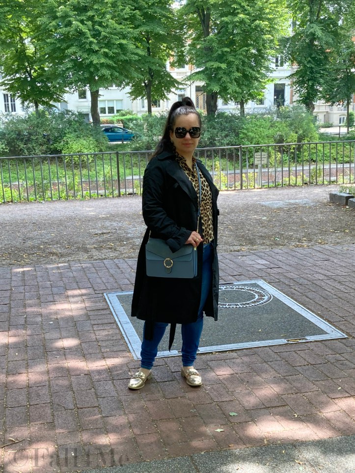 A black trench coat worn with skinny jeans and a leopard printed blouse.