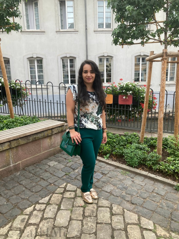 Green business pants combined with a white blouse with roses and leafs on it, a green cross body bag and golden accessories make the perfect urban jungle look.
