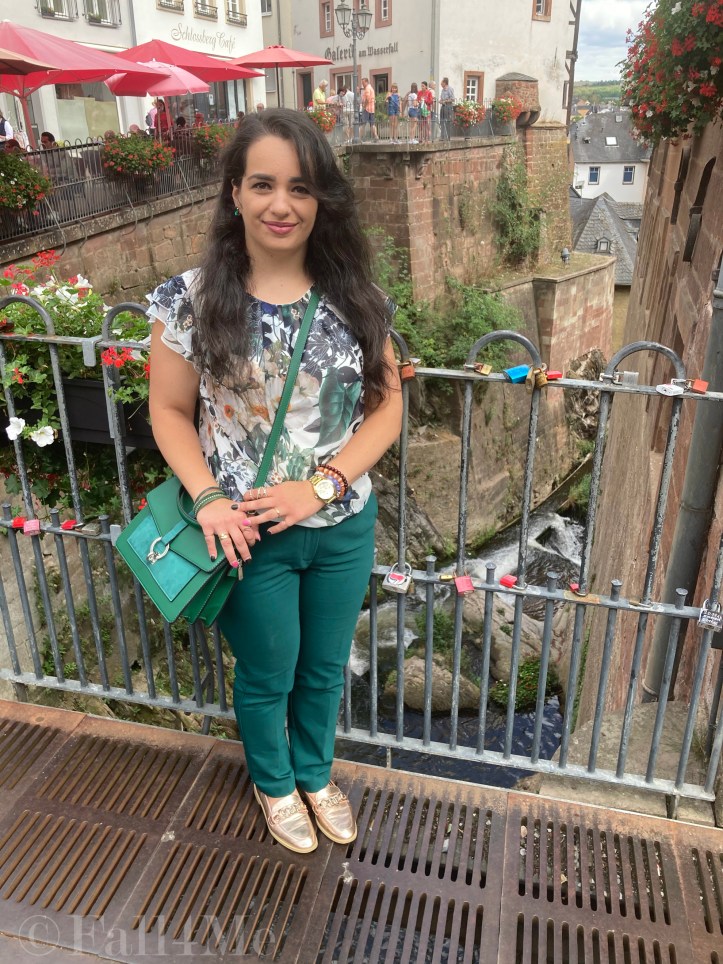 Green business pants combined with a white blouse with roses and leafs on it, a green cross body bag and golden accessories make the perfect urban jungle look.