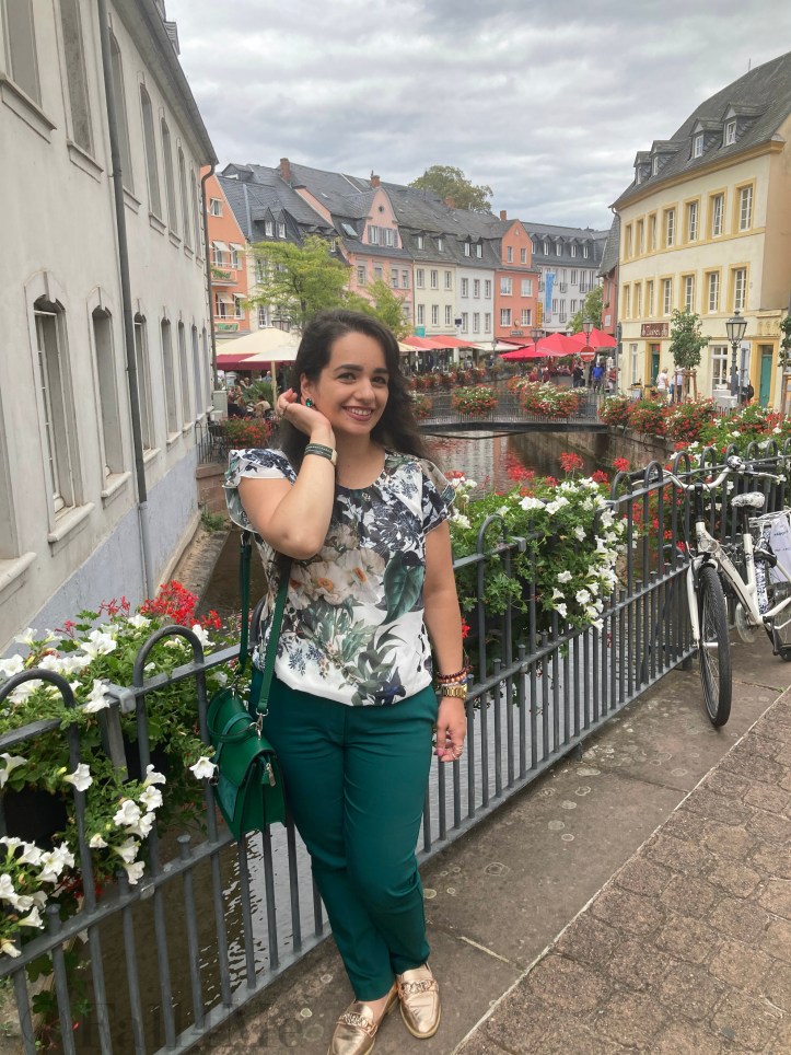 Green business pants combined with a white blouse with roses and leafs on it, a green cross body bag and golden accessories make the perfect urban jungle look.