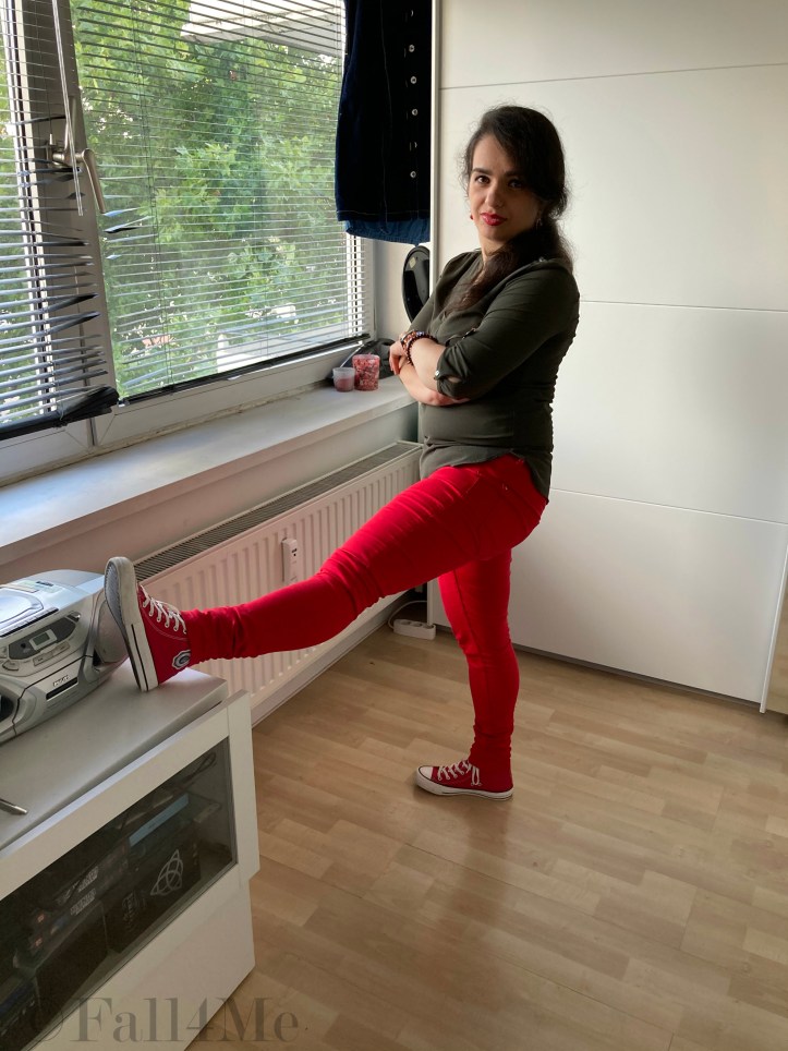 An olive green blouse combined with red lipstick and red skinny jeans and red chucks.