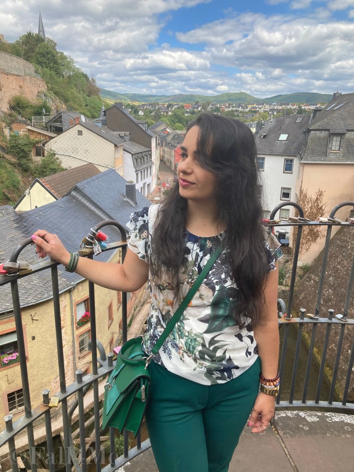 Green business pants combined with a white blouse with roses and leafs on it, a green cross body bag and golden accessories make the perfect urban jungle look.