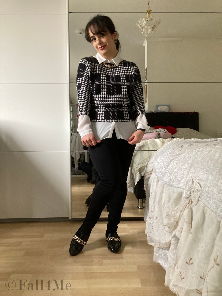 A shirt styled under a pullover in black and white with golden chain-accessories.