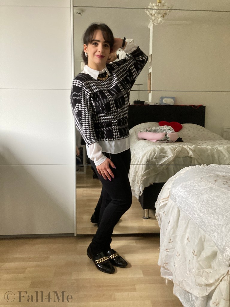 A shirt styled under a pullover in black and white with golden chain-accessories.