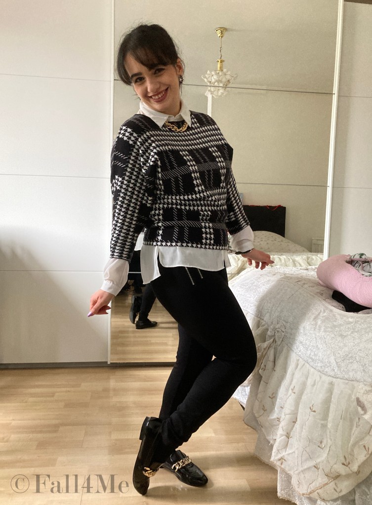 A shirt styled under a pullover in black and white with golden chain-accessories.