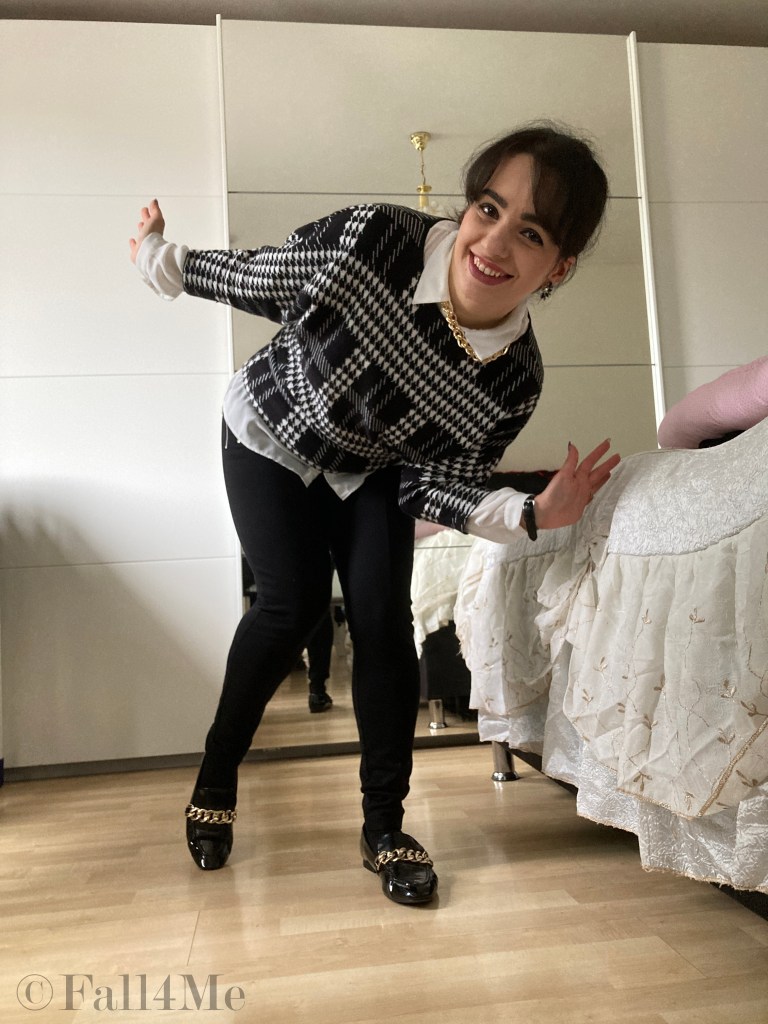 A shirt styled under a pullover in black and white with golden chainaccessories.