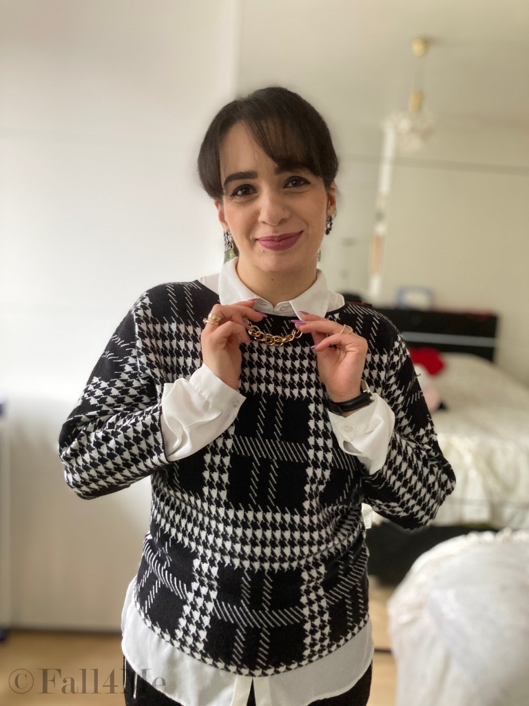 A shirt styled under a pullover in black and white with golden chainaccessories.