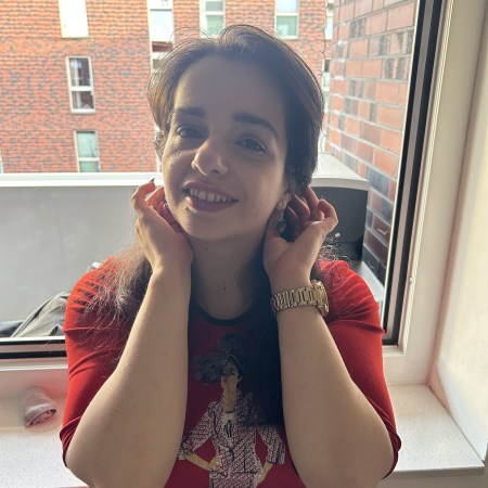 A pleated skirt making the skirt of the season worn with a black blazer, black over-knee-boots and red tights.